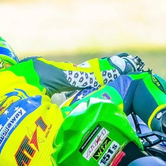 Rider in a fluo custom AT1 suit in a full racing tuck on track